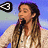 A pixelated image of a person with long brown hair holding a black microphone against a blue gradient background, featuring a small black and white symbol in the top-left corner.