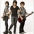 Three figures stand in a holding guitars, with the central figure wearing a black shirt and gray pants, flanked by two figures in gray shirts and dark pants
