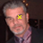 A 48x48 pixel animated contact sheet showing two frames of a man with gray hair wearing a purple shirt and dark jacket, with a yellow crosshair on his eye in the first frame that disappears in the second frame.