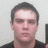 Static image of a person with short dark hair wearing a black shirt against a light gray background.
