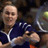 Pixelated static image of a person in dark blue athletic wear with white accents holding a tennis racket, set against an indistinct background.