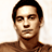 Pixelated static image of a person's face and upper shoulders with dark hair, neutral expression, and brown-toned skin against a light background.