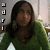 A static pixelated image shows a person with long dark hair wearing a green top against a light background with vertical elements.