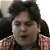 Static pixelated image of a person with dark hair and light skin wearing a checkered shirt, cropped to show upper body against a plain background.