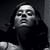 Pixelated grayscale image of a person with long dark hair, wearing a dark top against a dark background.
