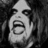 Pixelated grayscale image of a stylized face with an open mouth, triangular head shape, and dark eyes against a textured background.
