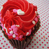 A cupcake with red frosting and heart-shaped sprinkles on a heart-patterned background.