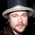 Pixelated close-up of a person wearing a dark top hat with a light band, light skin, and a mustache against a black background.