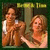 Two figures in warm-toned clothing stand near a vertical pole with green text above, set against a dark background.