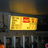 A pixelated yellow rectangular sign with red accents and partial text, set against a dark background with vertical elements below.