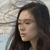 Pixelated close-up of a person with long dark hair against a blurred light background, showing partial facial features and clothing.