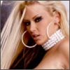 A close-up of a person with long blonde hair wearing large hoop earrings and a white beaded choker necklace, set against a dark background.