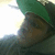Pixelated static image showing a partial figure with green and brown tones against a bright background.