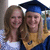 Two people in graduation attire pose closely together, one wearing a blue cap and gown with a yellow stole, the other in a white top.