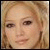 Pixelated close-up of a person's face with light brown hair and neutral expression on a beige background.