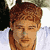 Static pixelated image of a person's face with brown hair and light skin, cropped to show only the head against a white background with partial dark and light elements on the sides.