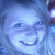 Pixelated blue-toned static image of a smiling face with closed eyes and visible teeth, set against a blurred background.