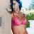 Pixelated image of a person with dark blue hair wearing a pink bikini top, standing outdoors with green foliage and light-colored background.