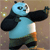 Pixelated cartoon panda in blue and black attire with arms extended, standing against a brown background with scattered light spots.