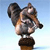 Pixelated image of a dog-like figure with large ears, brown and gray fur, standing on a brown base against a light blue gradient background.