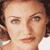 Pixelated close-up of a person's face with brown curly hair, visible eyes, nose, mouth, and partial ear against a white background.