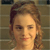Pixelated close-up of a person with light brown hair styled in a side part, wearing a light-colored top against a muted striped background.