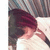 Pixelated image of a person with dark red hair wearing a dark top, head tilted down, and hand near face against a blurred background.
