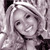Pixelated grayscale image of a smiling person with light hair, wearing a dark top, against a patterned background.