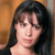 Pixelated close-up of a person with dark shoulder-length hair against a warm-toned background, static image with no visible text or props.