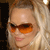 Pixelated close-up of a person with light-colored hair wearing orange-tinted sunglasses, set against a dark background with a light area on the right.