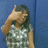 A pixelated figure with dark hair wears a light-colored shirt with white patterns, raising one hand near their face against a solid blue background.