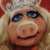 Pixelated close-up of a pig-like character with light brown fur, blue eyes, and a silver crown, smiling against a red background.