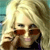 Pixelated image of a person with light-colored hair holding a dark object near their face against a blurred background.