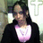 A pixelated static image shows a person with dark hair wearing a black jacket over a white shirt with a pink design, standing against a blurred background with light and dark tones.