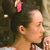 A pixelated close-up of a person's head and shoulder with dark hair, a light-colored shirt, and a pink object above the head against a dark background.