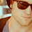 A person wearing dark sunglasses and a gray tank top, with a red heart symbol appearing on the right cheek in one frame.