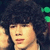 A person with dark curly hair and light skin appears in a of four , with green circular lights visible in the background