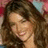 Pixelated close-up of a person with long brown hair, light skin, and a neutral expression against a blurred background with red and blue tones.