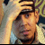 Pixelated static image of a person's face with visible facial features and partial clothing, rendered in warm tones on a light background.