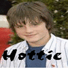 A person with light brown hair and glasses wears a white pinstriped jacket over a blue shirt, with the word 'Hottie' in bold black text overlaid on the lower portion of the image.
