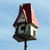 Pixelated birdhouse icon with dark red roof, gray body, and white accents on a light blue background.