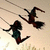 Two anime-style figures on swings against a light background with faint grass-like lines; one figure has long dark hair and teal clothing, the other is darker silhouetted.