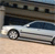 A silver sedan with dark tinted windows is parked in front of a building with a stone facade and dark rectangular windows.