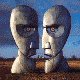 Two stylized stone heads face each other against a blue sky and brown field background, with subtle facial expression changes across frames.