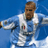 Pixelated static image of a soccer player in motion wearing a white jersey with blue accents and red/black details on the chest, set against a solid blue background.