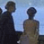 Pixelated static image of two humanoid figures standing side-by-side against a light blue background, with visible dithering and low-resolution rendering artifacts.