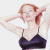 A pixelated image of a person with light brown hair wearing a dark blue spaghetti-strap top, hands behind head against white background.