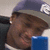 A person wearing a dark blue cap with white text, holding a blue rectangular object near their face in a of four
