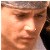 Pixelated close-up of a person's face with light skin tone, brown eyes, and dark hair, wearing a dark jacket over a light shirt.