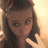 A pixelated image of a person with long brown hair and a headband, making a peace sign against a light background with pink text elements.